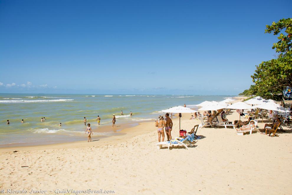 Imagem de pessoas curtindo as águas claras e no guarda-sol na Praia de Apaga Fogo.